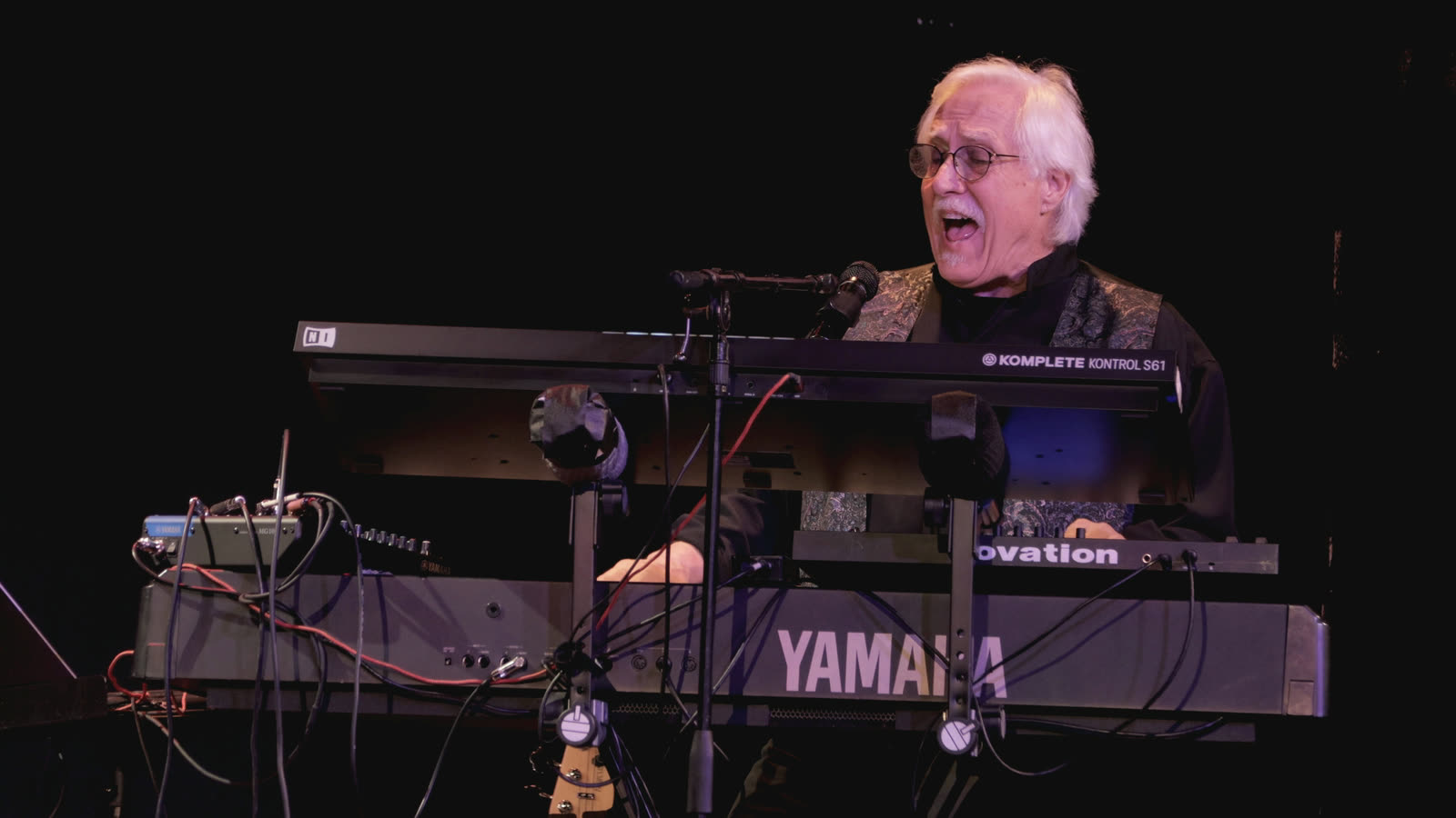 Rico singing at the microphone behind his keyboards.