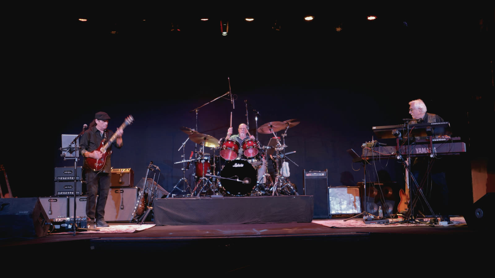 Allen playing a red guitar at left, with Ed on drums and Rico at the keyboards.